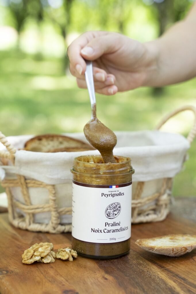 Cuillère de praliné de noix caramélisées au-dessus du pot, avec une corbeille de pain grillé